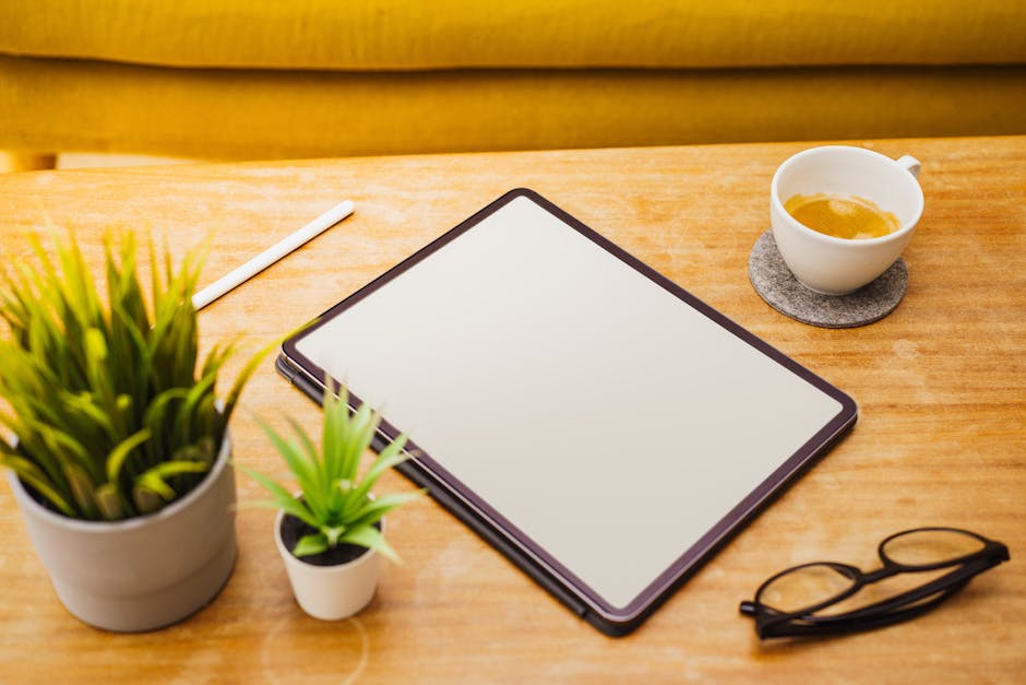 A clean workspace featuring a digital tablet, coffee cup, plants, and eyeglasses on a wooden table.