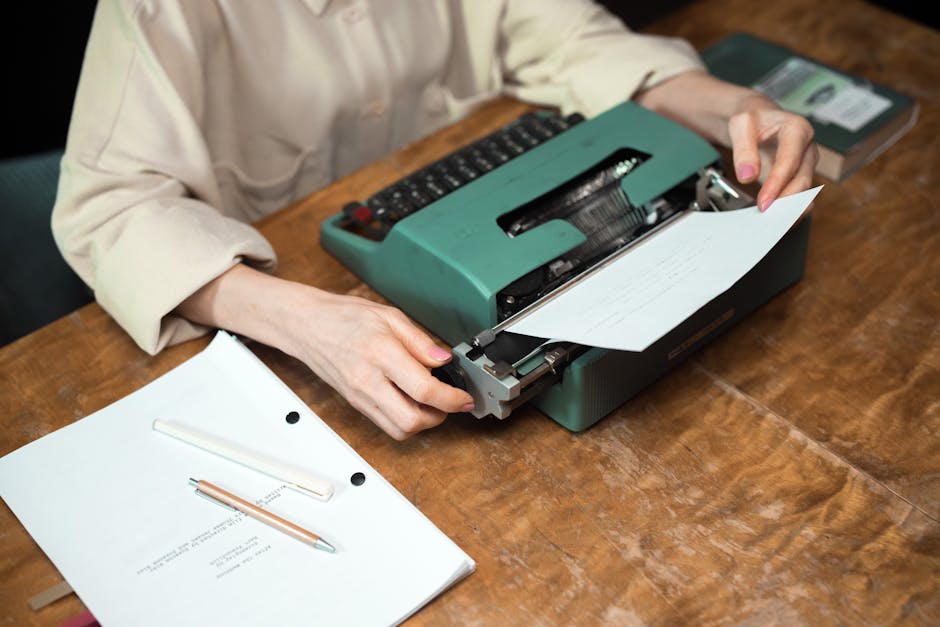 Close-up of hands using a vintage typewriter, with paper and script on a wooden desk.
